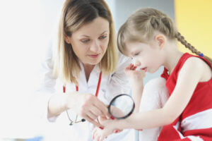 a pediatric dermatologist examining skin on hand of little girl using magnifying glass